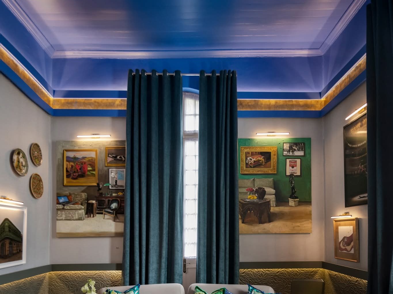 Sala presentada en Casacor 2025, con cornisa azul, galería de cuadros y sofá curvo